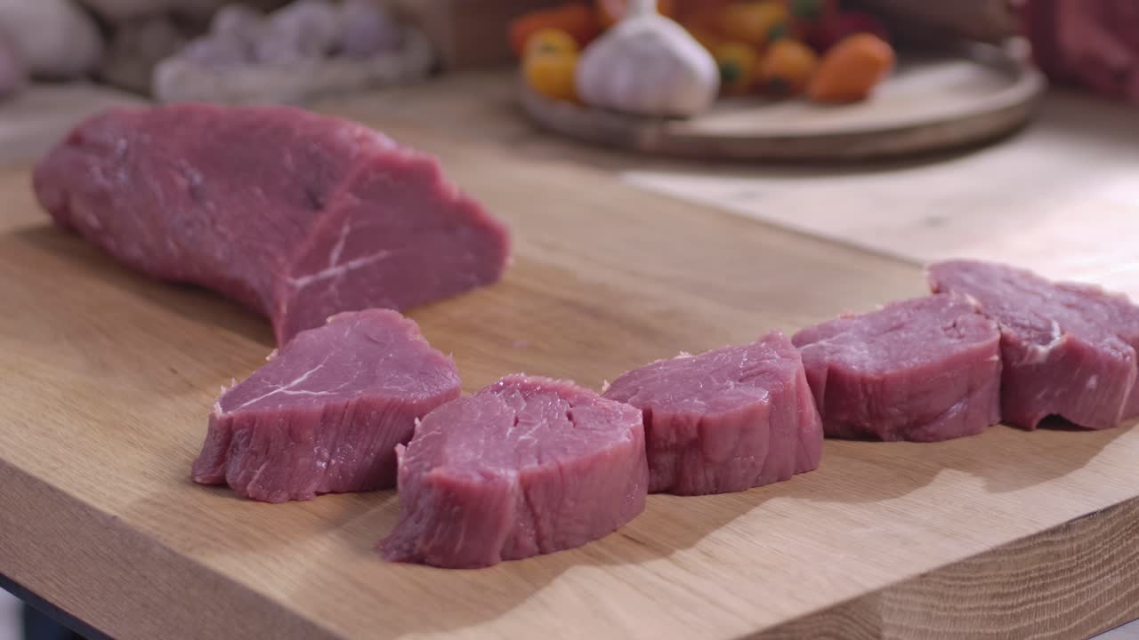 Close up seorang koki yang mengenakan sarung tangan hitam mengiris daging sapi tanpa lemak mentah segar menjadi steak di atas talenan kayu di dapur