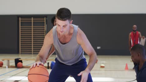 diverse male basketball players dribbling ball and falling during game at indoor court, slow motion