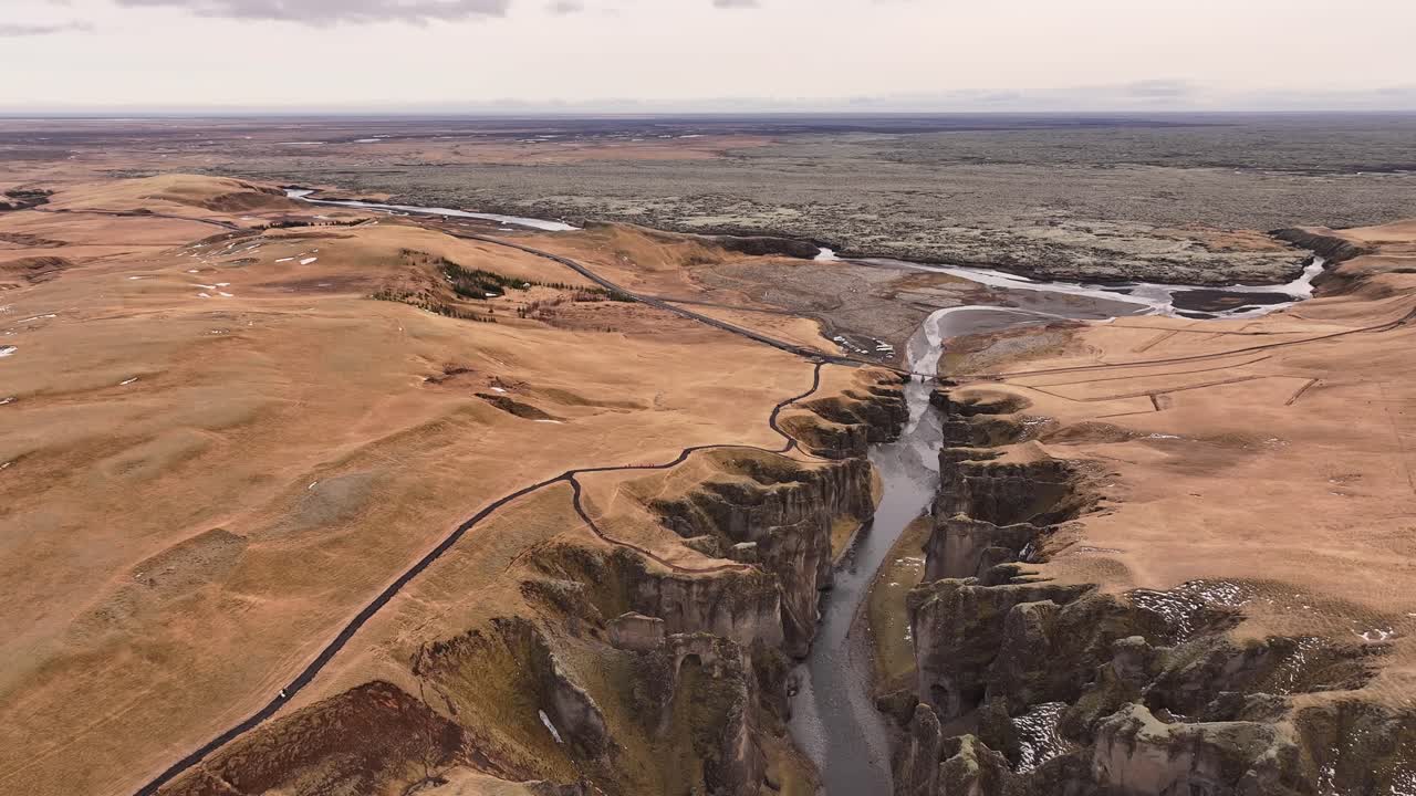 Drone flying over Fjaðrárgljúfur Canyon, showing the deep river gorge surrounded by golden fields near Kirkjubæjarklaustur, Iceland.