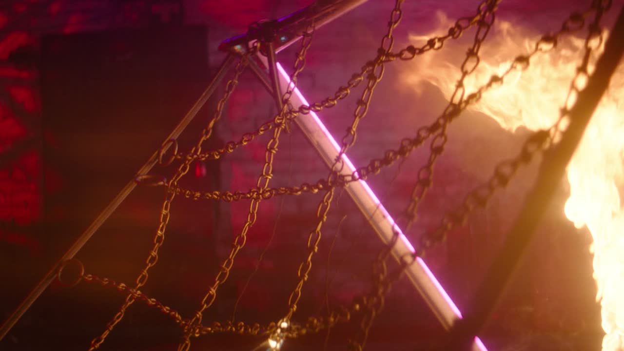 Intenso filmato cinematografico di un canestro da basket con rete a catena avvolto da fiamme drammatiche, con un pallone all'interno del cerchio. Un vivido raggio laser viola taglia diagonalmente la scena, creando una potenza
