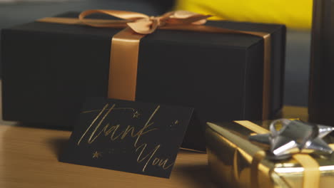 Close-Up-Of-Thank-You-Card-Next-To-Gift-Wrapped-Presents-On-Table-In-Lounge-At-Home