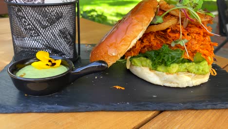 Juicy-pulled-chicken-burger-with-onion-rings,-avocado,-crispy-kale,-brioche-bun-and-sweet-potato-french-fries,-fast-food-restaurant-with-nature-view,-4K-shot