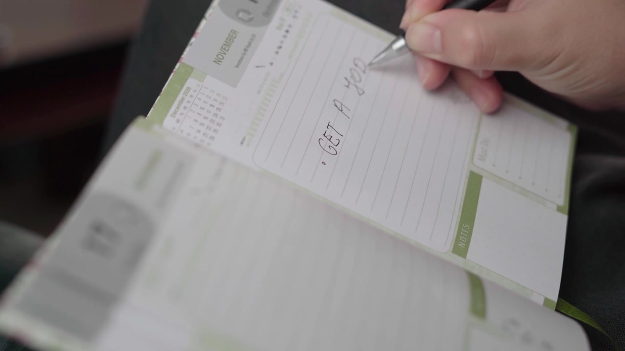 Primo piano di una persona che scrive un promemoria per la ricerca di lavoro in un'agenda personale di novembre con luce interna soffusa