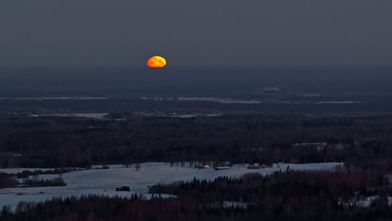 Orange måne står op over et snedækket landskab i skumringen og skaber en fredfyldt stemning.