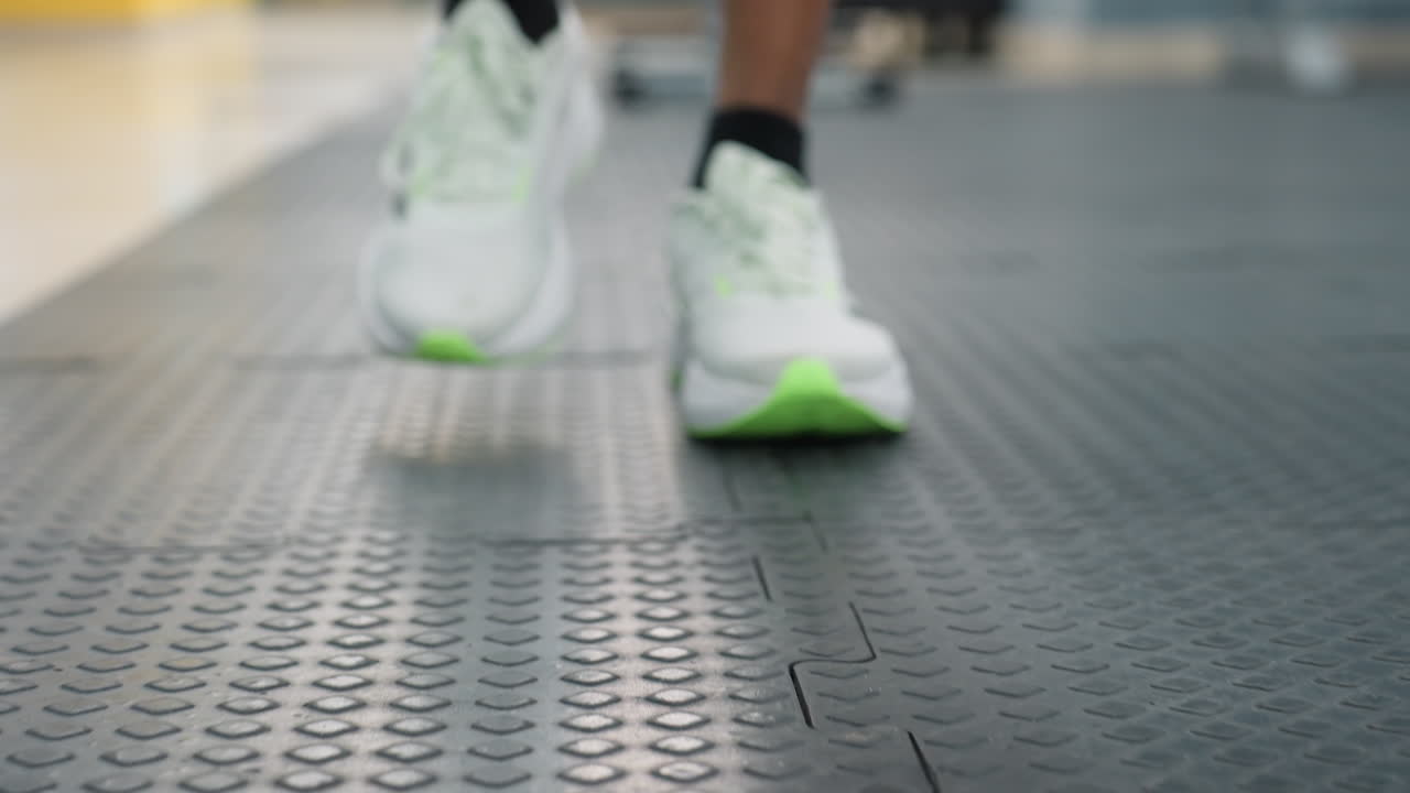 close up of white and green sneakers stepping on interlocking rubber gym mats with blurred weight machines and bright windows in background