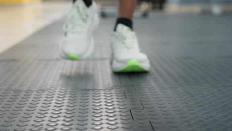 close up of white and green sneakers stepping on interlocking rubber gym mats with blurred weight machines and bright windows in background