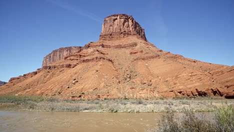 en una cálida mañana soleada de primavera cerca de moab, utah, se ve una impresionante montaña de piedra arenisca naranja con el río colorado debajo.