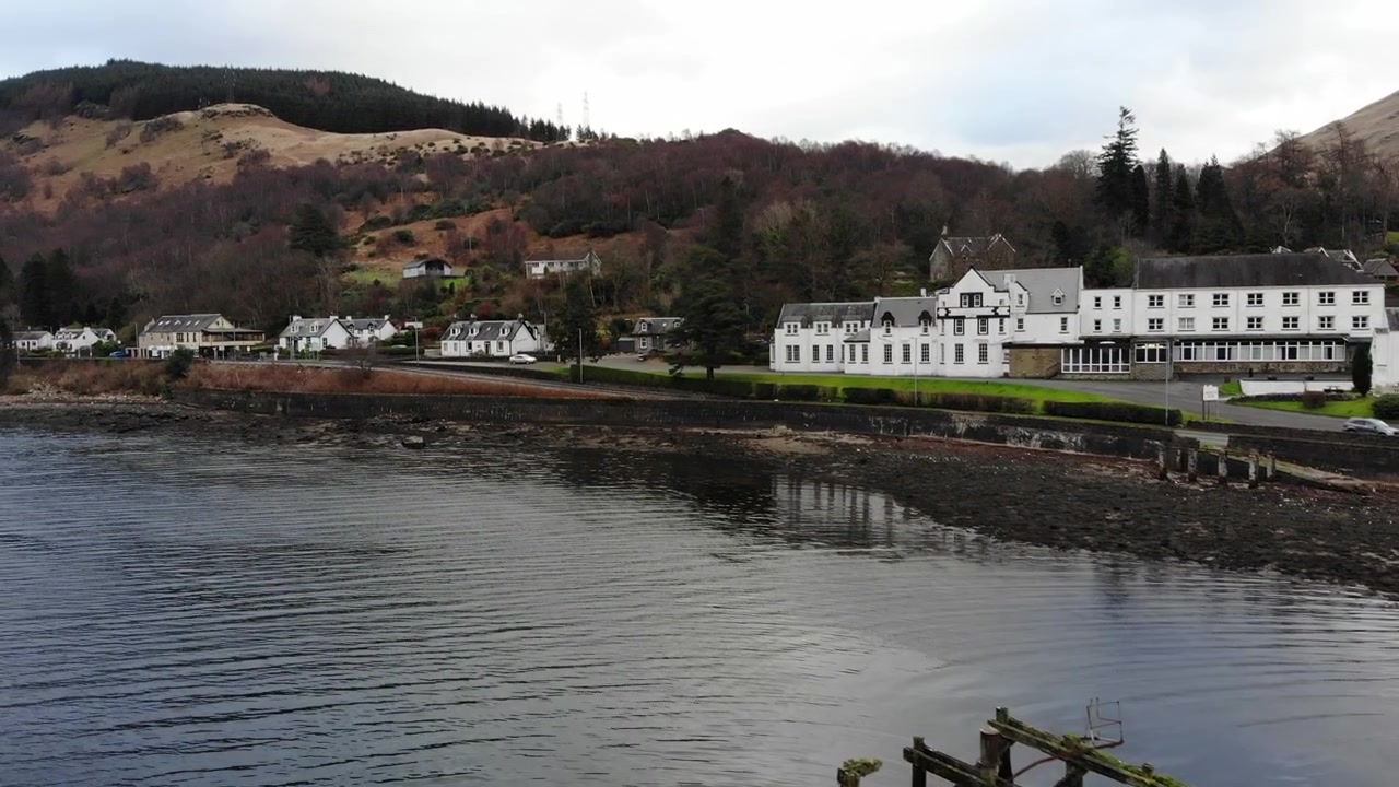 Vista drone in ascesa che rivela il vecchio molo di legno di Arrochar e il paesaggio del lungo loch scozzese