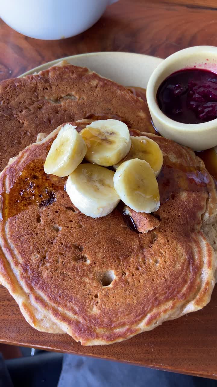 Maple syrup is poured on pancake with banana for breakfast in cafe or restaurant. Fancy bistro shop with delicious menu filmed from phone pov of foodie person or influencer eating out in city downtown