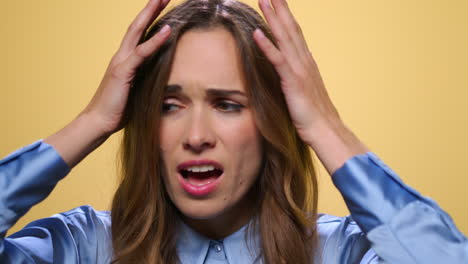 stressed woman standing on yellow background. woman touching head with hands