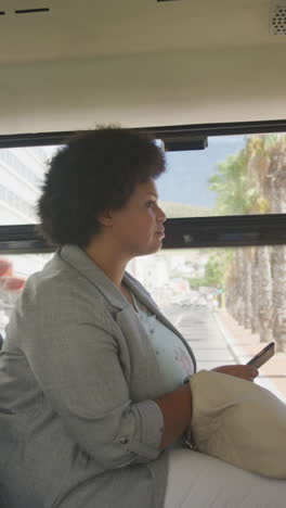 vertical video of plus size biracial woman using smartphone in bus