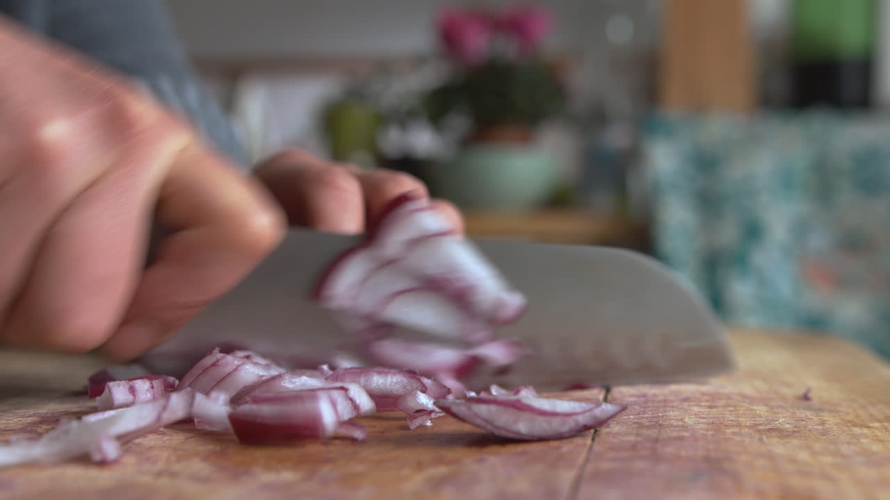 Close up woman's hand fast chopping in pieces Italian red onions with a rounded sharp knife in the kitchen