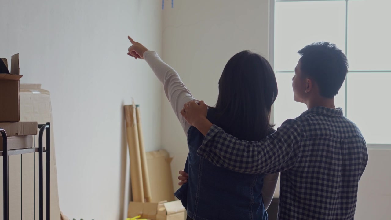Couple with their arms around each other standing in room and dreaming about decorating new home
