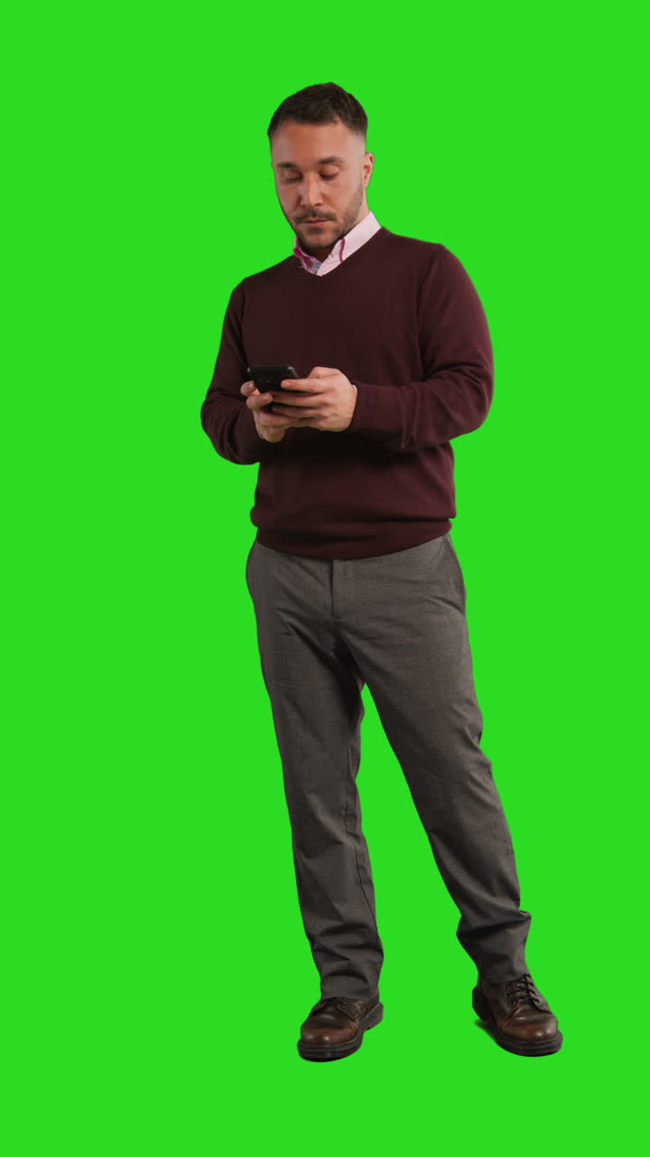 video verticale di lunghezza completa girato in studio di un uomo d'affari che usa il telefono cellulare per inviare messaggi o navigare online in piedi contro la schermata verde 1