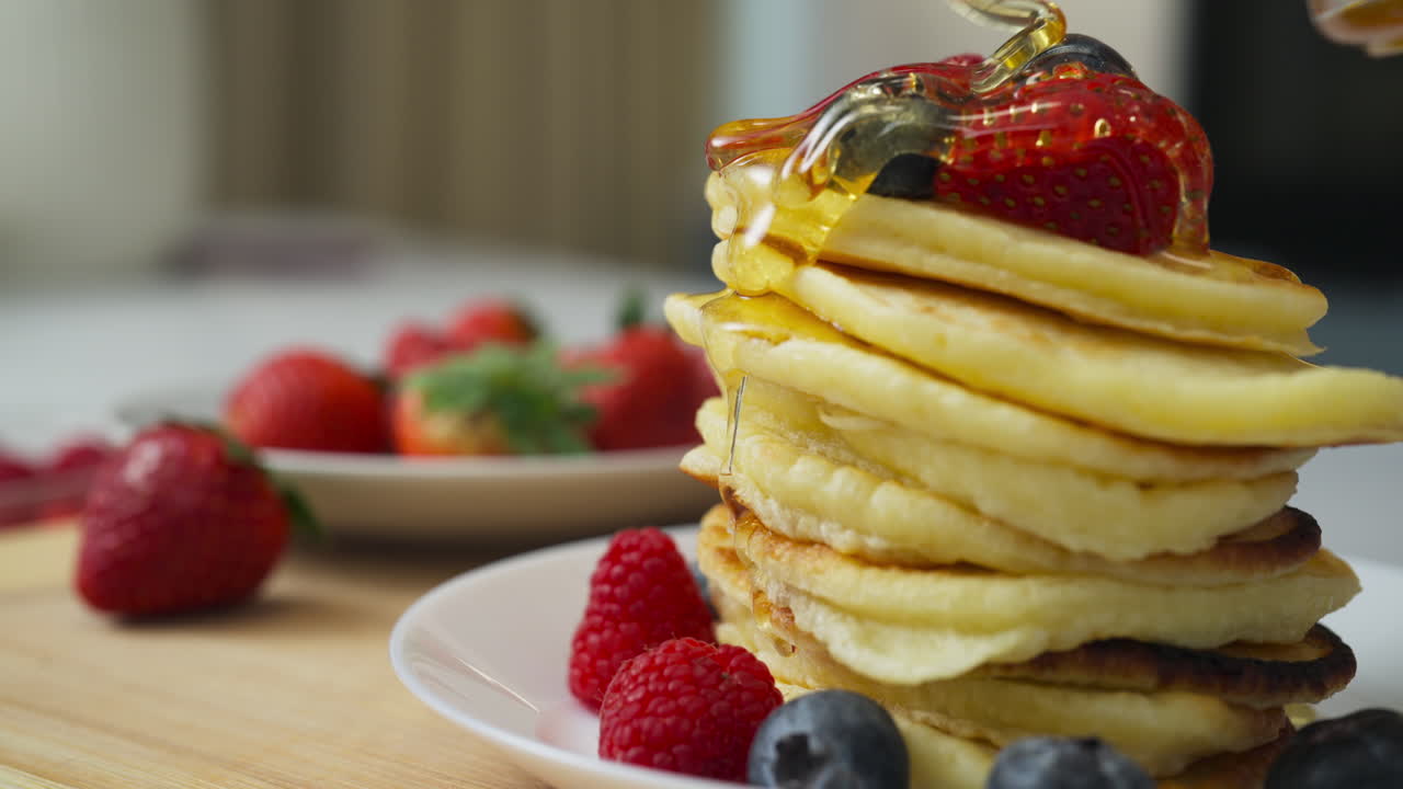 Pouring honey on healthy homemade pancakes with fruit in slow motion