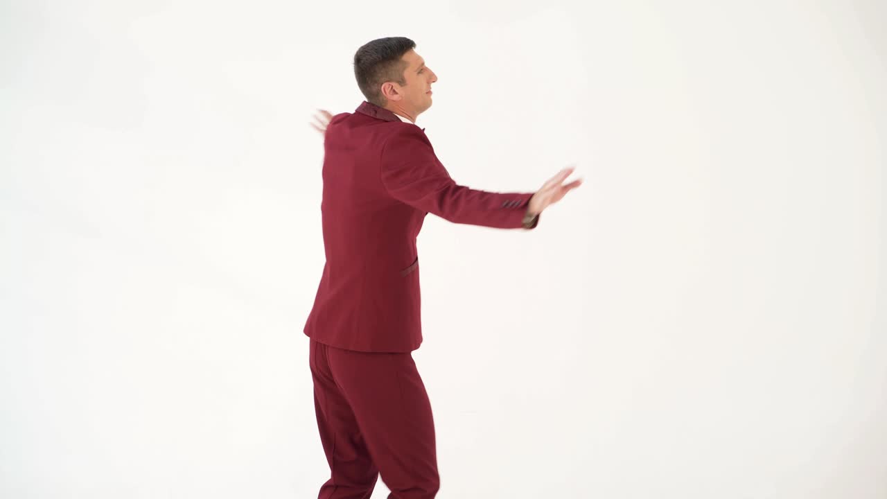 fun showman in red suit is waving his arms and spinning around himself on a white background in the studio