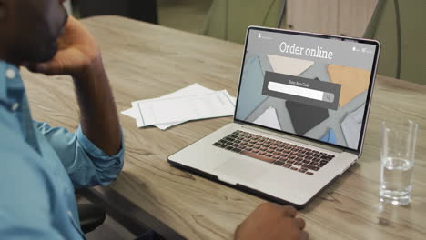 African-american-man-at-table-using-laptop,-online-shopping-for-clothes,-slow-motion