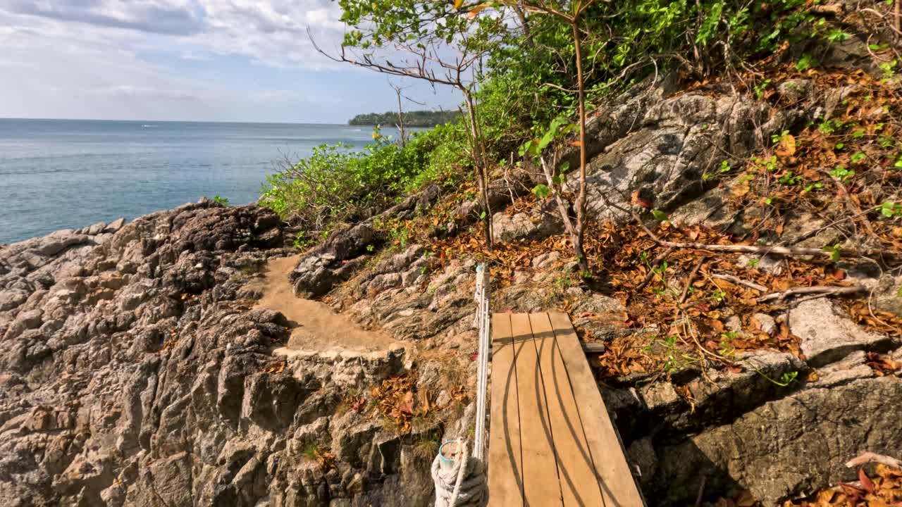 A serene coastal path with wooden bridges and rocky terrain under bright daylight, offering stunning ocean views
