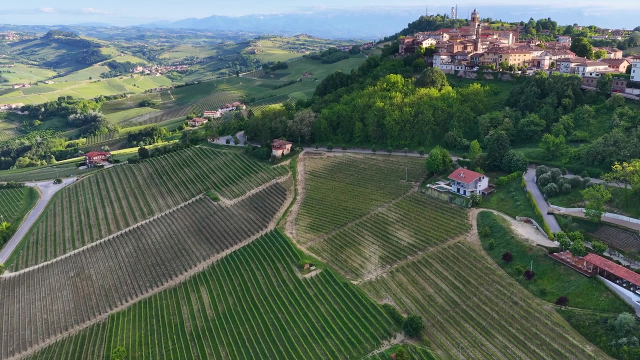 Volo veloce di drone su verdi colline ondulate e vigneti verso un borgo italiano storico in cima a una collina.
