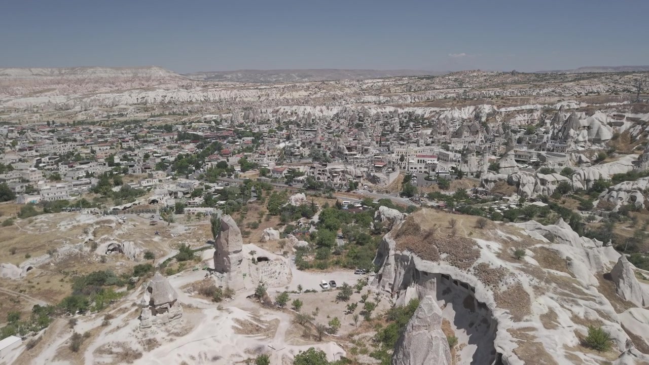 Arka planda merkezi Göreme kasabasıyla peri bacalarının üzerinde 4K 10-bit yukarıdan drone çekimi. Açık gökyüzü altında kaya oluşumlarının ve şehir vadisinin güneşli bir yaz günü havadan panoramik görüntüleri.