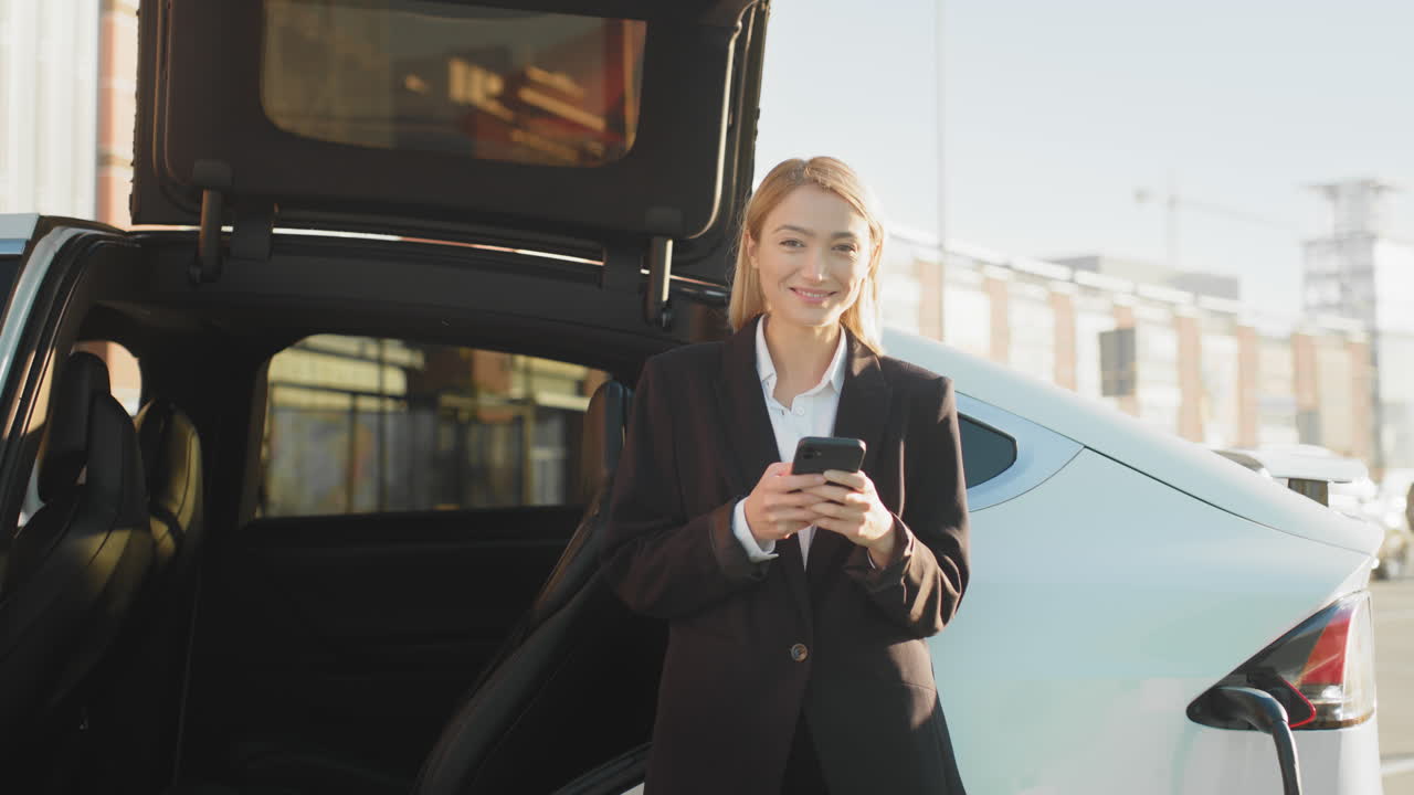 mujer de negocios usando el teléfono cerca del coche eléctrico