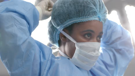 african american female surgeon wearing face mask in operating theatre, slow motion