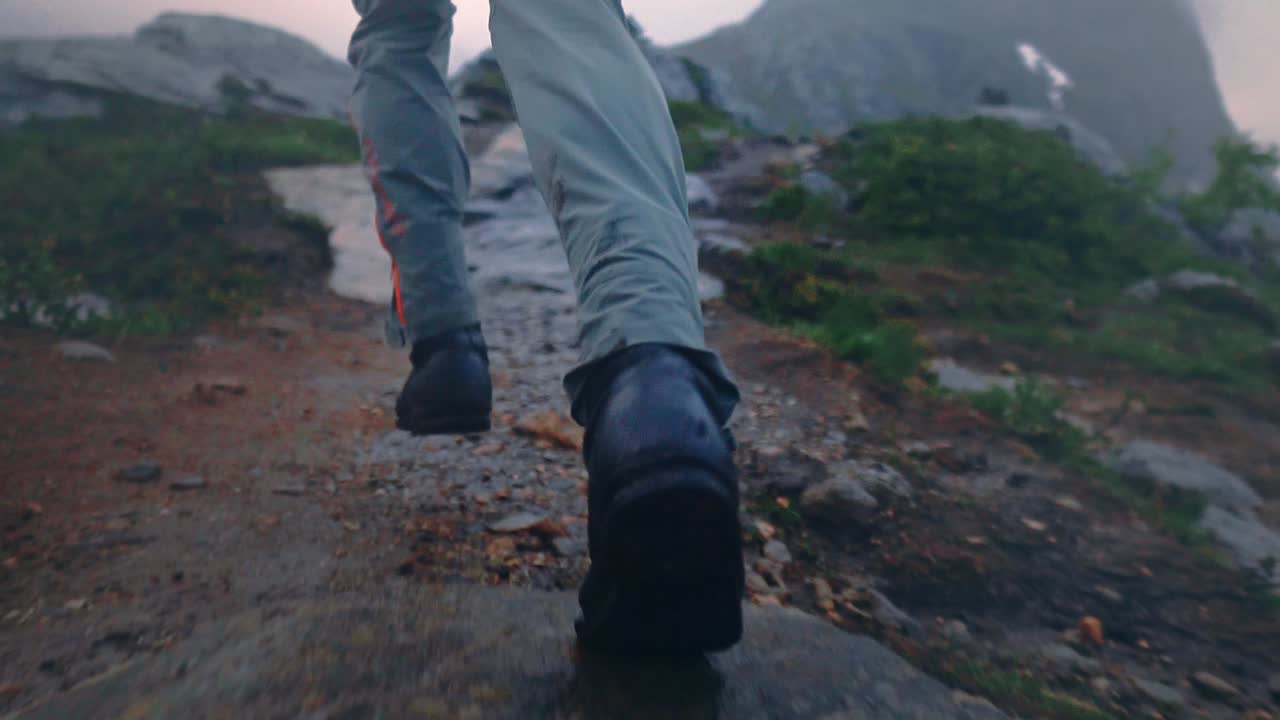 Slow motion shot of person running over rocky terrain, on top of a mountain.