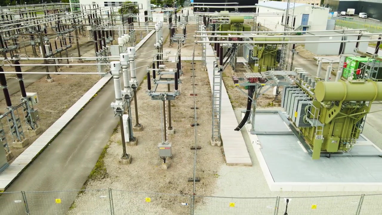 Prospettiva aerea di una sottostazione elettrica ad alta tensione con linee elettriche, isolatori e trasformatori, che mostra una moderna rete elettrica e infrastruttura di distribuzione dell'energia dall'alto.