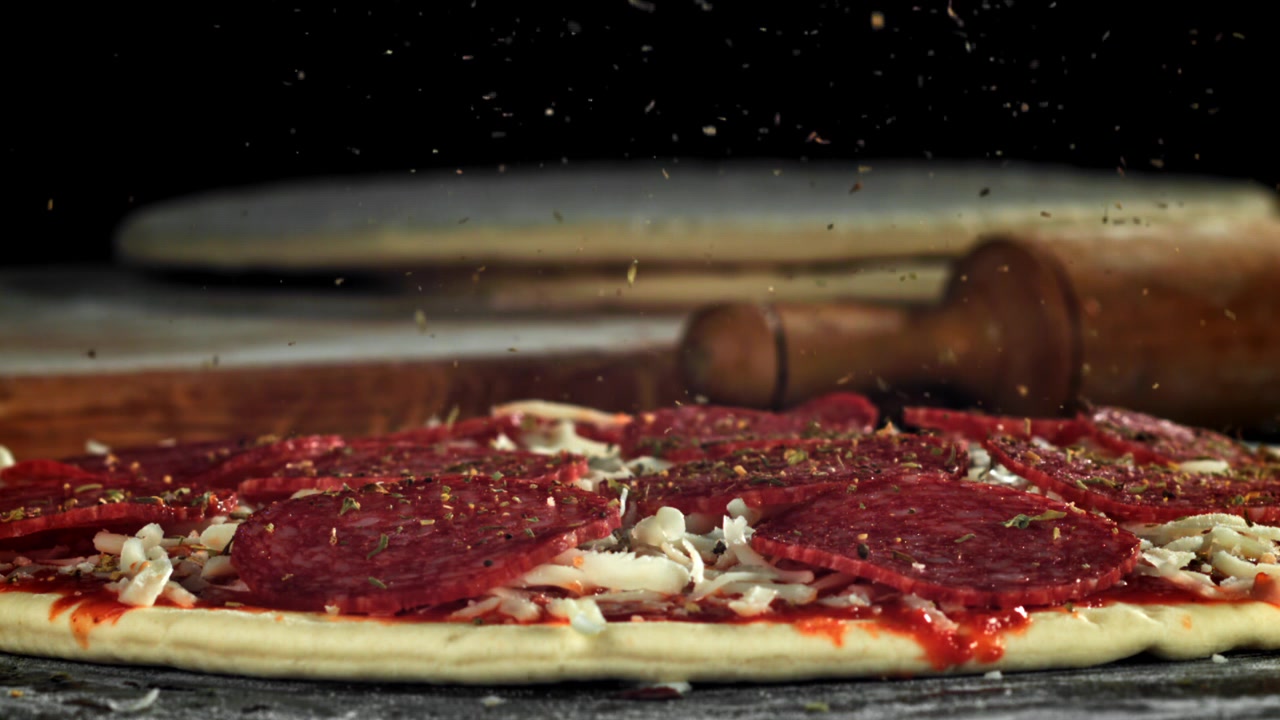 Movimento rallentato di erbe aromatiche cosparse su una pizza con salame piccante cruda