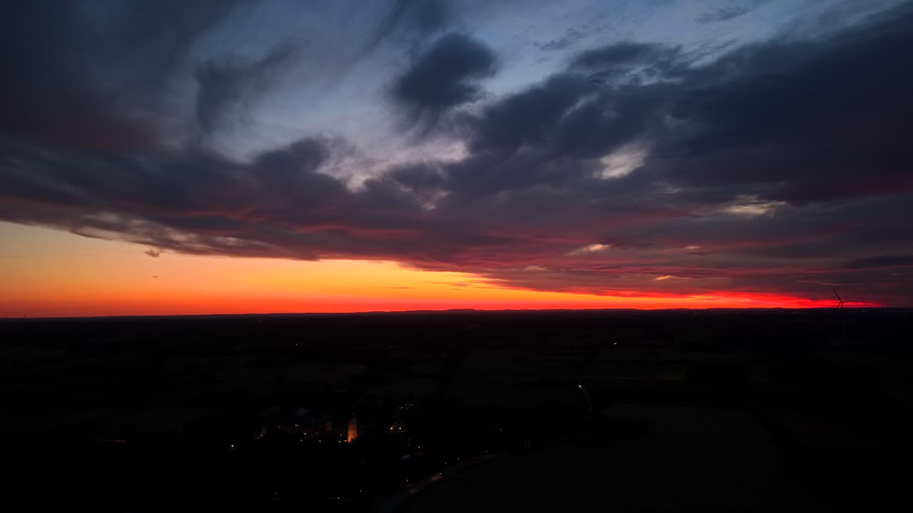 Dramatic sunrise sky with orange colors and mystic clouds in America. Small American town with church tower and cars on road in the morning. Aerial wide shot. Blue hour scene