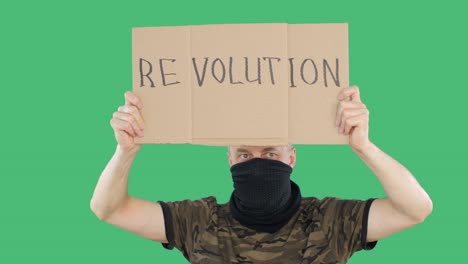 military man in camouflage shirt and facial bandana with revolution poster on green screen background. protester man with cardboard with revolution inscription raised hands up on green background.