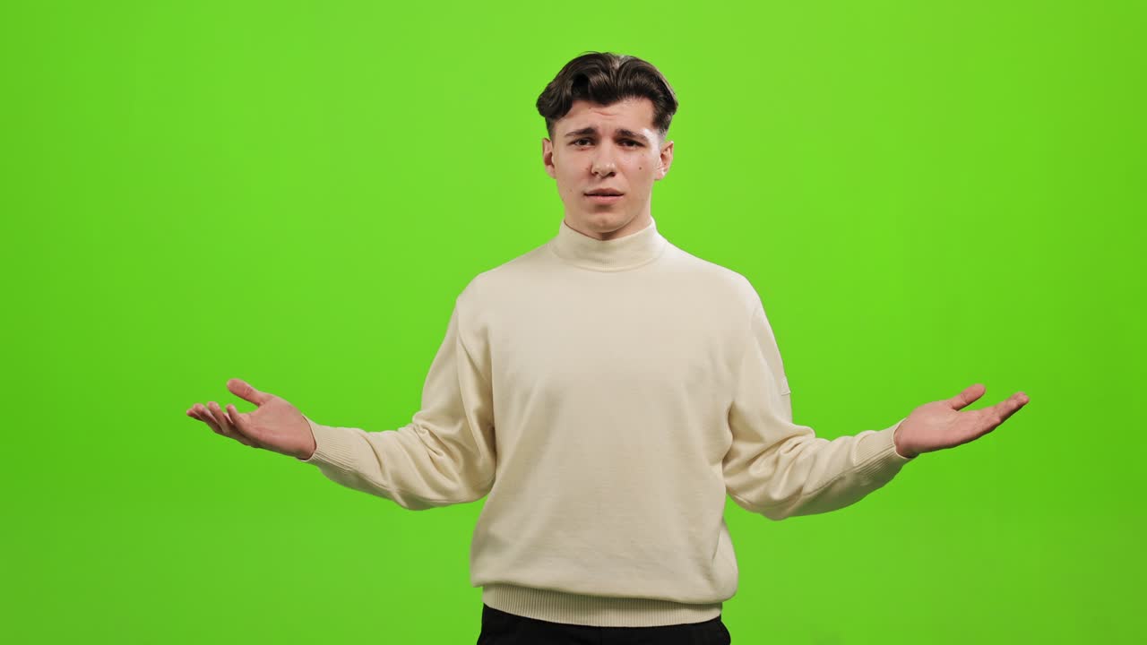 The man is standing and looking at the camera. He is raising his hands and asking - What. He is standing on a green background. Green screen. 4K.
