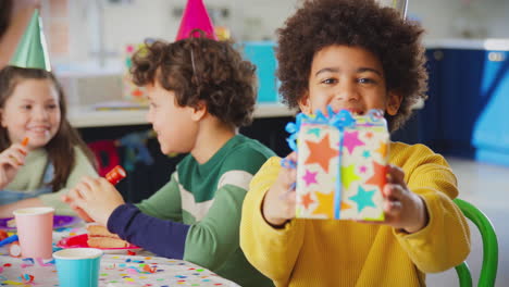 Boy-Giving-Gift-At-Birthday-Party-With-Friends-And-Parents-At-Home