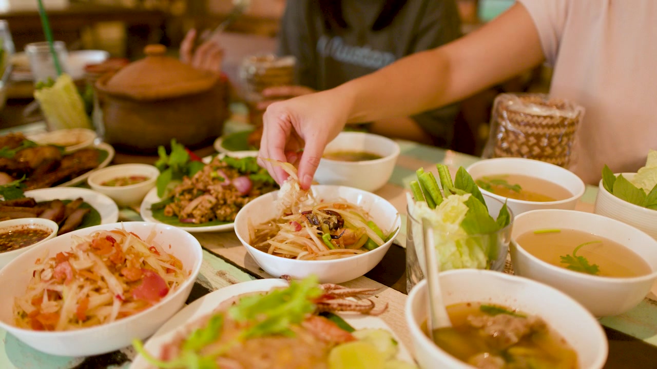 Close-up tangan mencocol nasi ketan ke dalam salad pepaya pedas di sebuah restoran di Bangkok