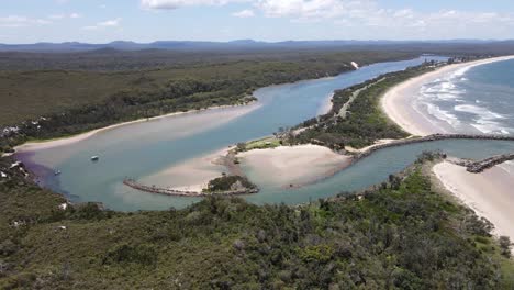 aerial view of a peaceful coastal inlet with a jetty, where a river flows into the ocean, surrounded by lush greenery and sandy shores, showcasing nature's beauty
