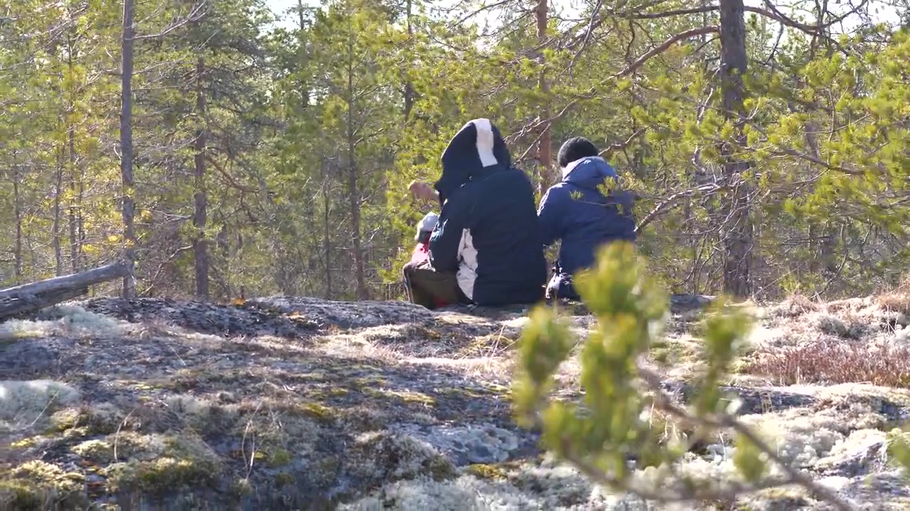 Familie i flere generationer vandrer i skoven og sidder sammen på en klippe.
