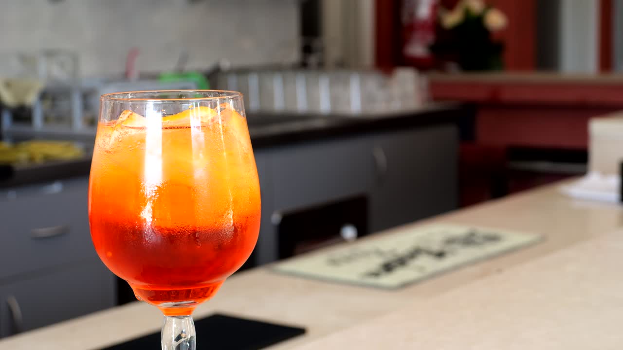 Close-up of soda being poured into a glass of Aperol Spritz with ice and orange slices, captured during cocktail preparation on a bar counter