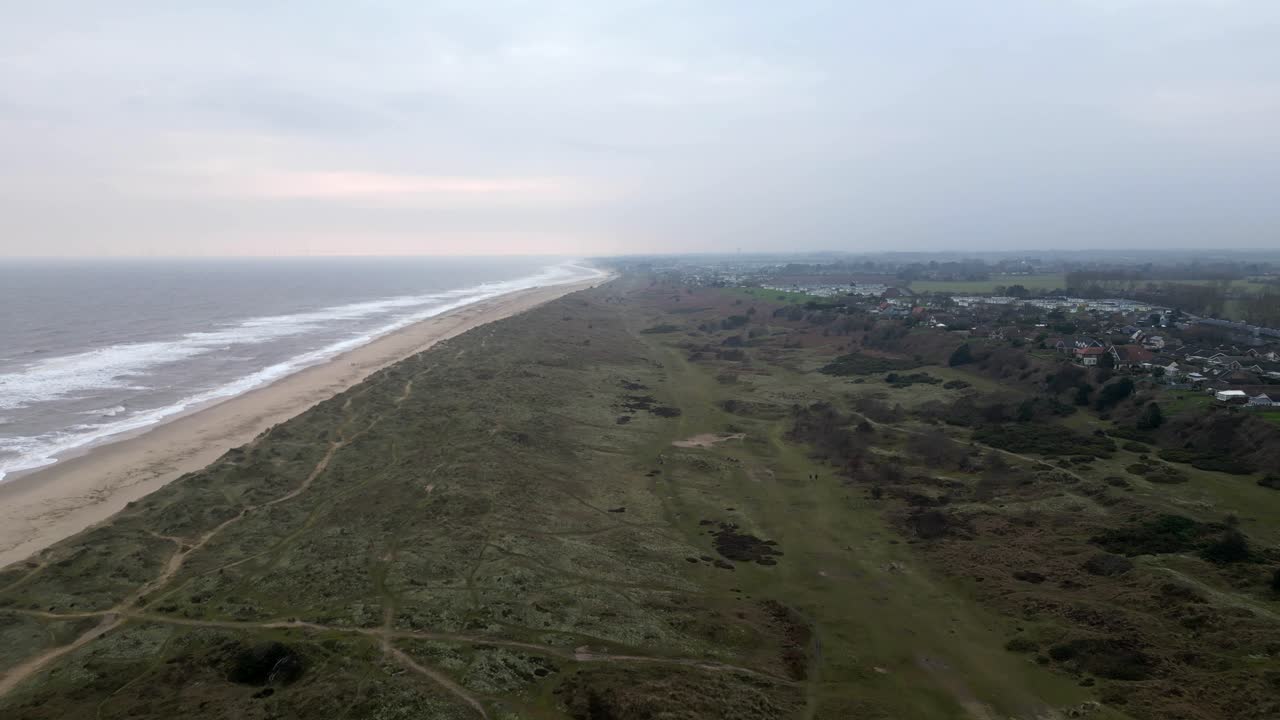 Drone dolly shot over dunes revealing coastline and Winterton village at dusk