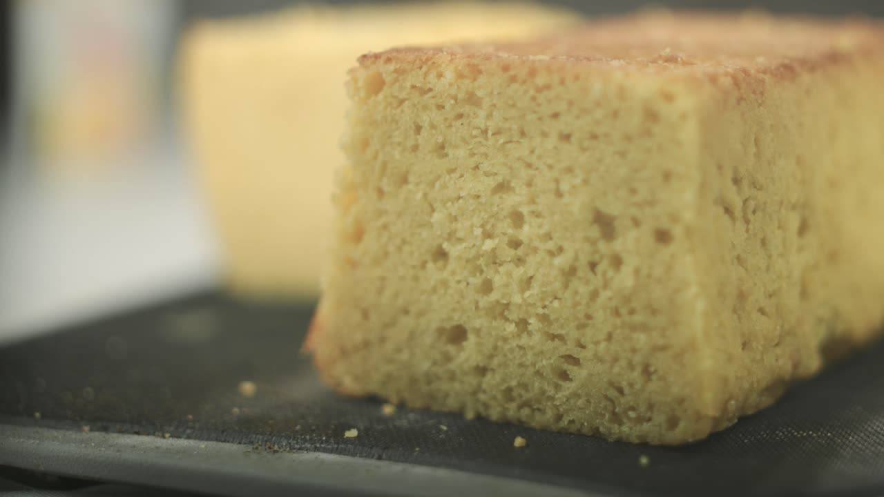 Uno chef che testa la consistenza di una torta pan di Spagna appena sfornata, con un pezzo di torta tagliato in primo piano