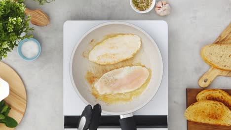 crop person frying chicken fillet in pan in kitchen