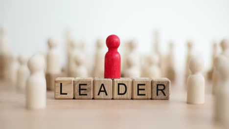 a red leader figure stands on "leader" blocks among other wooden figures, symbolizing leadership and prominence