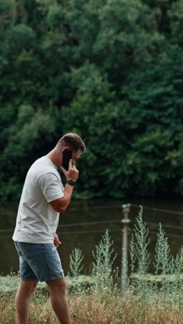 man using a phone outdoors near a river and forest