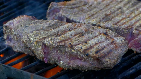 two juicy rib eye steaks cooking on the grill as fire and flames shoot up down below