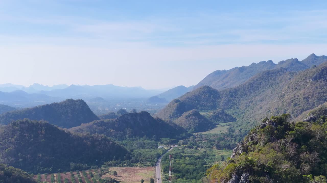 Uma foto aérea ampla com drone captura montanhas tropicais exuberantes e uma estrada sinuosa sob a luz do dia