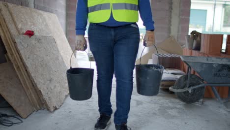 4k cámara lenta de primer plano de dos cubos llevados por un trabajador mientras sube las escaleras en un sitio de construcción, mostrando la carga y el esfuerzo.