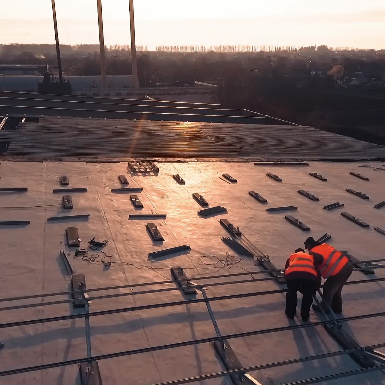 Metal basis for solar panels on roof. Workers installing special equipment for sunny models on a rooftop at sunset. Aerial view.