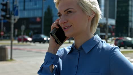 joven mujer de negocios en una camisa azul hablando en el centro de la ciudad en un teléfono móvil