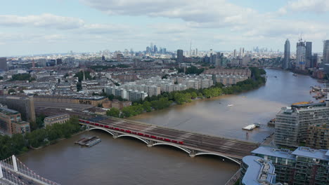 Aerial-panoramic-view-of-Thames-river-flowing-through-city.-Train-driving-on-multi-track-Grosvenor-Railway-Bridge.-London,-UK