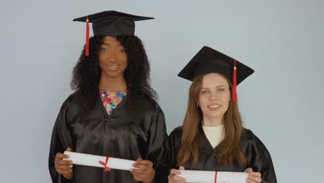 young african american and caucasian women stand on assignment and hold horizontal diplomas