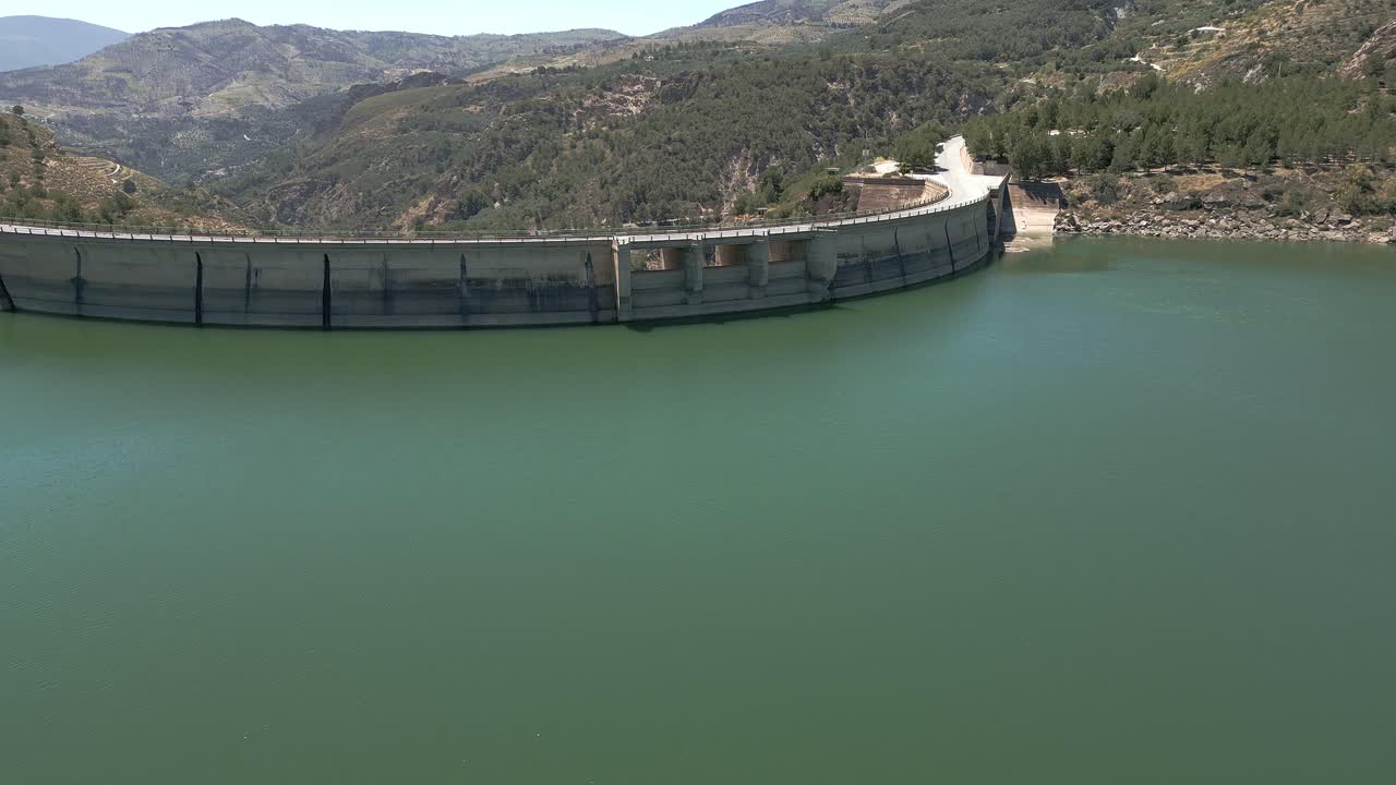 Vault dam. Dam spillway. Reservoir. Aerial view of road over curved dam. Spain.